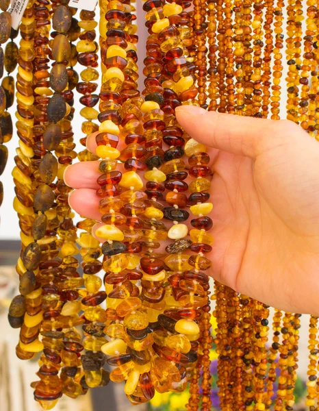 Mão de mulher com colares de âmbar femininos brilhantes na barraca no bazar — Fotografia de Stock