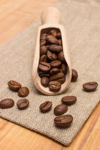 Куча кофейных зерен с деревянной сенсацией на холсте джута на столе — стоковое фото