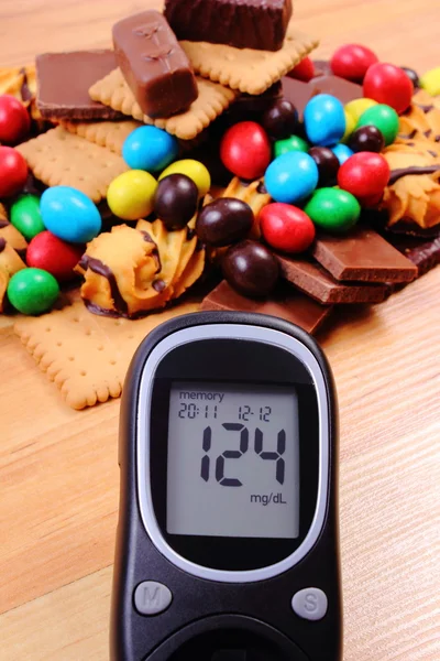 Glucometer con un montón de dulces en la superficie de madera, diabetes y alimentos poco saludables — Foto de Stock