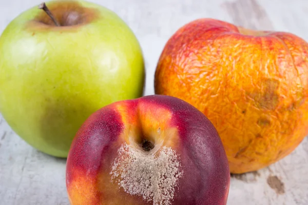 Spoiled peach and apple on old wooden white table — Stock Photo, Image