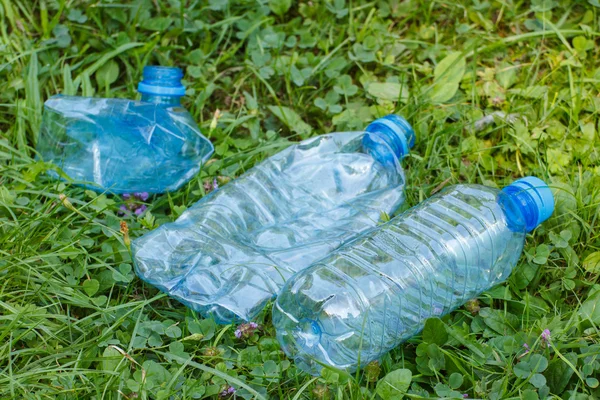 Plastic bottles of mineral water on grass in park, littering of environment — Stock Photo, Image