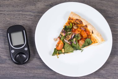 Glukometre, taze pişmiş vejetaryen pizzayla şeker seviyesini ölçmek ve kontrol etmek için kullanılır. Diyabet konsepti sırasında besin