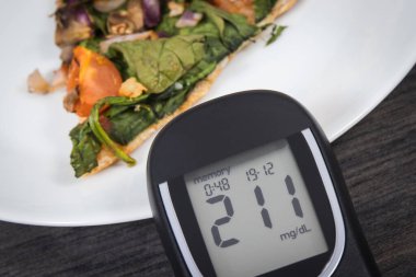 Glukometre, şeker seviyesi ve taze pişmiş vejetaryen pizzanın çok yüksek bir sonucu. Diyabet konsepti sırasında besin