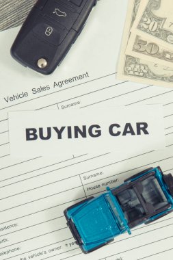 Küçük mavi oyuncak araba, siyah anahtar, dolar banknotları ve bir çeşit araç satış anlaşması. Araba satın alma yazıtları. Satışlar ve yeni ya da kullanılmış araba alımları