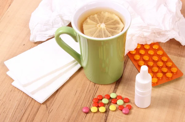 Comprimidos e gotas de nariz para resfriados, lenços e chá quente com limão — Fotografia de Stock
