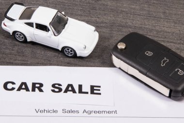 Küçük beyaz oyuncak araba, siyah araba anahtarı ve bir çeşit araç satış anlaşması. Araba satışı. Satışlar ya da alımlar yeni ya da kullanılmış araçlar. Ulaşım