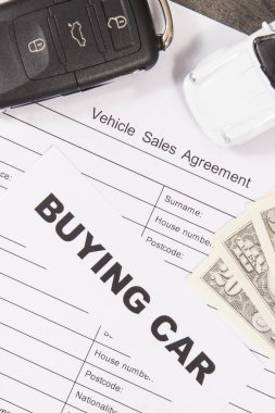 Küçük beyaz oyuncak araba, siyah araba anahtarı, dolar banknotları ve bir çeşit araç satış anlaşması. Satışlar ya da alımlar yeni ya da kullanılmış araçlar. Ulaşım