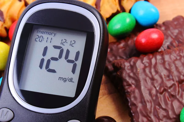 Glucose meter with heap of sweets, diabetes and unhealthy food — Stok fotoğraf