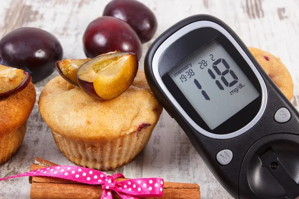 Glucómetro, panecillos con ciruelas y canela sobre fondo de madera, la diabetes y el delicioso postre — Foto de Stock