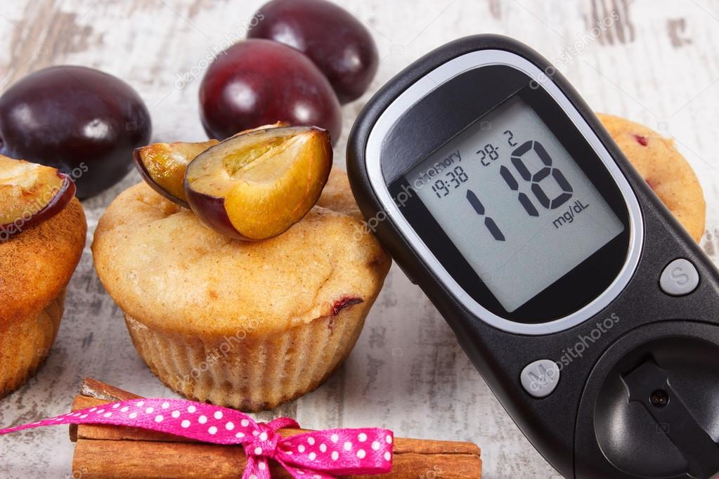 Glucometer, muffins with plums and cinnamon sticks on wooden background, diabetes and delicious dessert