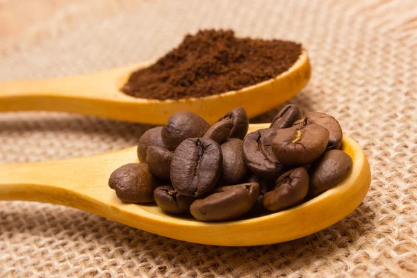 Grains and ground coffee with wooden spoon on jute canvas — Stock Photo, Image