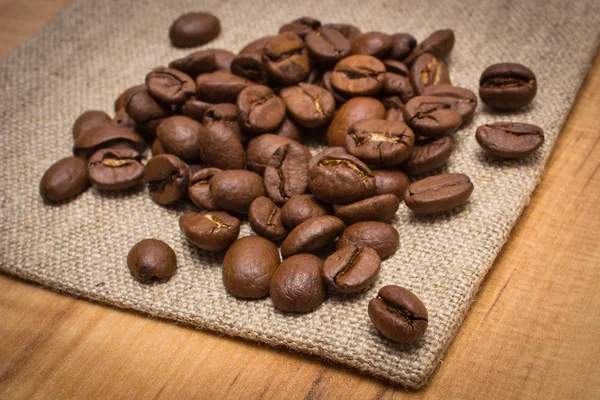 Haufen Kaffeebohnen auf Jutespralinen auf dem Tisch — Stockfoto