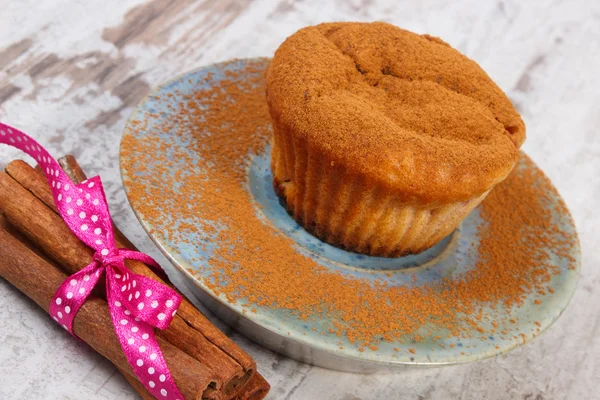 Muffiny s práškové skořice, skořicových tyčinek na dřevěné pozadí, lahodný dezert — Stock fotografie