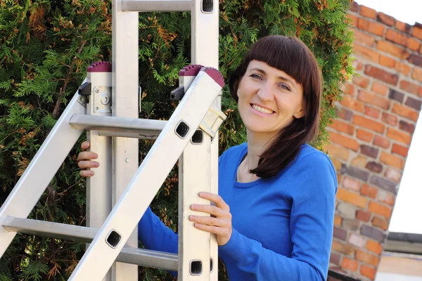 Mujer sonriente subiendo en escalera de aluminio en el jardín —  Fotos de Stock