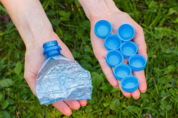 Mano de mujer con tapones de botellas y botellas de plástico, basura del medio ambiente — Foto de Stock