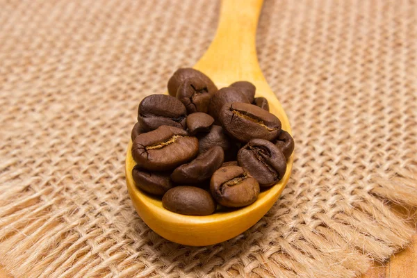 Haufen Kaffeebohnen mit Holzlöffel auf Jutescreme — Stockfoto