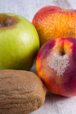 Spoiled kiwi, peach and apple on old wooden white table