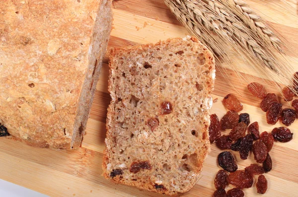 Pão fresco assado, espigas de trigo e passas — Fotografia de Stock