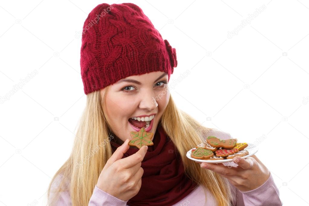 Happy woman in woolen cap and shawl eating gingerbread cookies, white background, christmas time