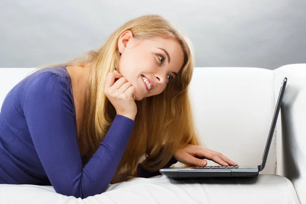 Mulher feliz deitada no sofá e usando laptop, tecnologia moderna — Fotografia de Stock