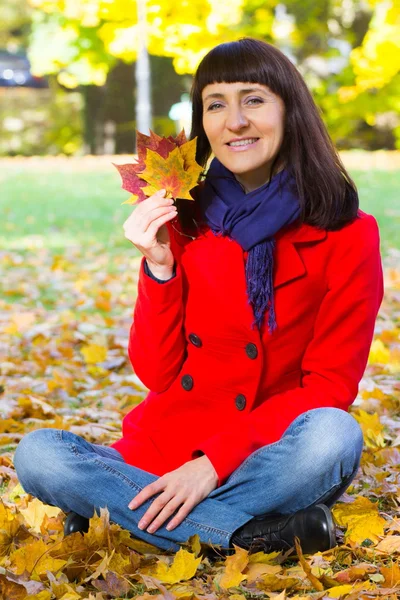 Mulher sorridente no parque outonal segurando folhas coloridas nas mãos — Fotografia de Stock