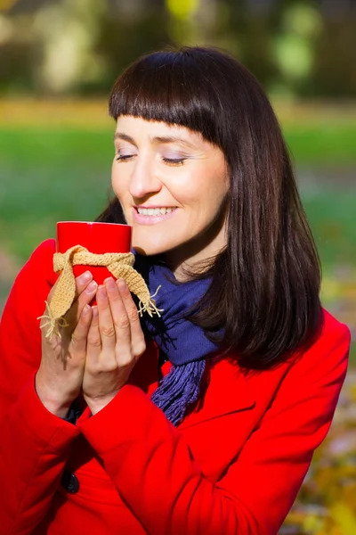 Mujer feliz sosteniendo taza de té caliente en el parque otoñal, otoño — Foto de Stock