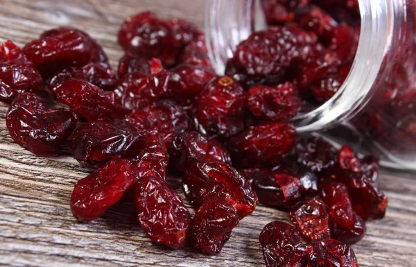 Cranberries spilling out of glass jar on wooden table — Stock Photo, Image