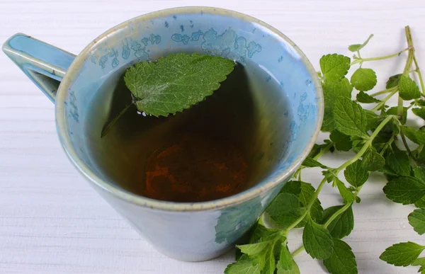 Frischer Melisse und Tasse Kräutergetränk auf weißem Holztisch — Stockfoto