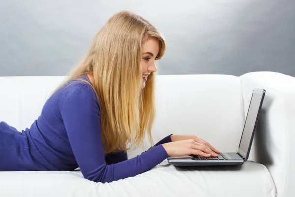Счастливая женщина использует ноутбук, лежащий на диване, современные технологии — стоковое фото
