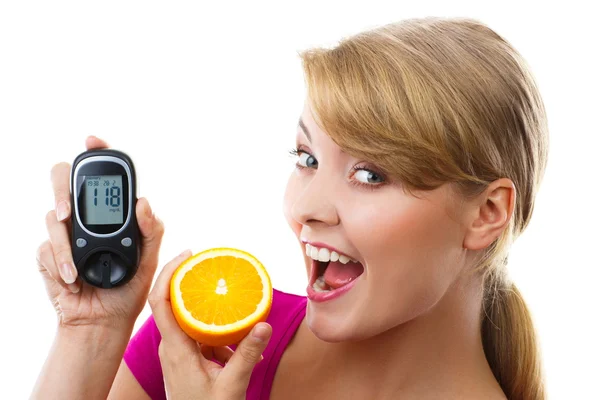 Happy woman holding glucometer and eating fresh orange, measuring and checking sugar level, concept of diabetes — Stock Photo, Image