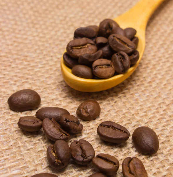 Heap of coffee beans with wooden spoon on jute canvas — Stock Photo, Image