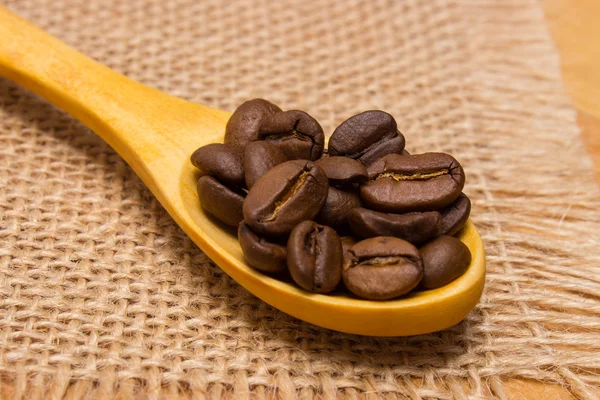 Högen av kaffebönor med träsked på jute duk — Stockfoto