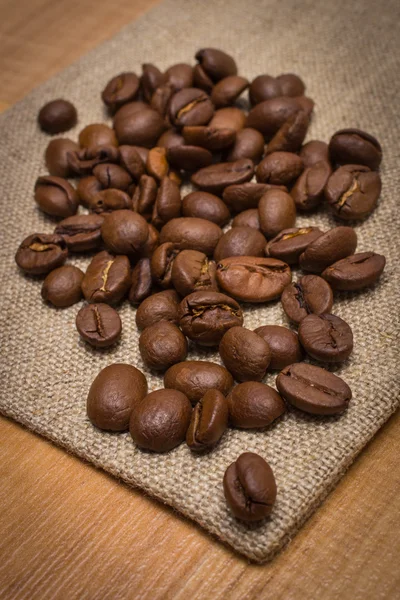 Un mucchio di chicchi di caffè su tela di iuta sul tavolo — Foto Stock