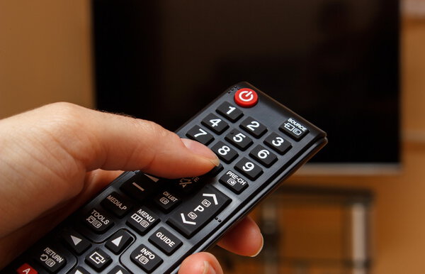 Hand holding remote control for television, choosing channel in TV