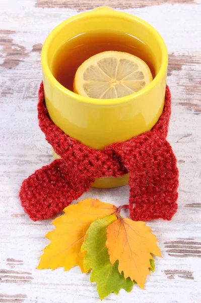 Taza de té caliente con pañuelo de lana envuelto en limón y hojas otoñales, bebida caliente para la gripe — Foto de Stock