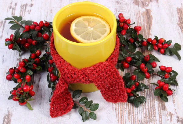 Cup of hot tea with lemon wrapped woolen scarf and cotoneaster, warming beverage for flu — Stock Photo, Image