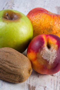 Spoiled kiwi, peach and apple on old wooden white table
