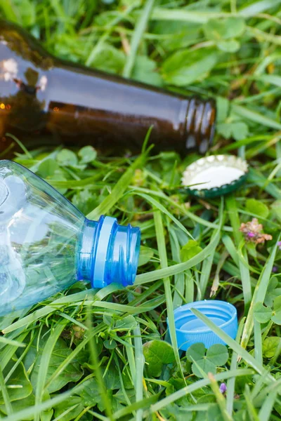 Plastic and glass bottle with bottle caps on grass in park, littering of environment — Stock Photo, Image