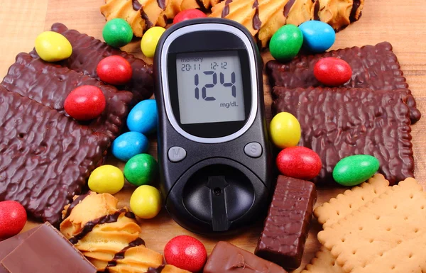 Glucometer com montão de doces na superfície de madeira, diabetes e alimentos insalubres — Fotografia de Stock
