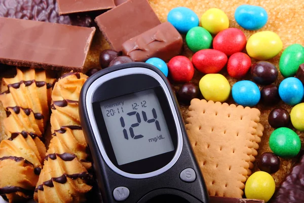 Glucometer with heap of sweets and cane brown sugar, unhealthy food — Stock Photo, Image