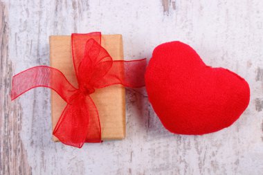 Wrapped gift for Valentines day and red heart on old wooden plank