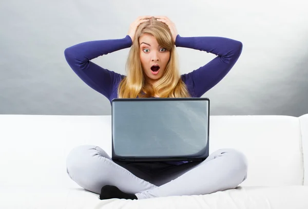 Испуганная женщина сидит на диване и смотрит на ноутбук, современные технологии — стоковое фото