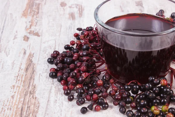 Bunch of fresh elderberry with juice on old wooden background, healthy nutrition — Stock Photo, Image