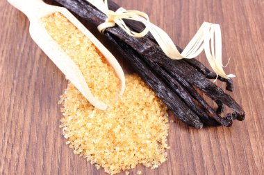 Sugar cane on spoon and fragrant vanilla sticks on wooden surface plank