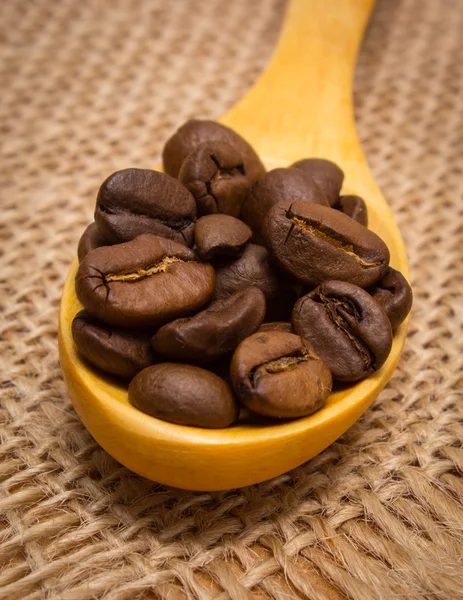 Haufen Kaffeebohnen mit Holzlöffel auf Jutescreme — Stockfoto