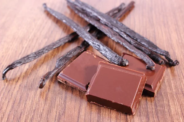 Donkere chocolade en geurige vanille stokjes op houten oppervlak plank — Stockfoto