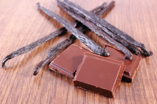 Chocolate negro y palos de vainilla fragantes en tablón de madera —  Fotos de Stock