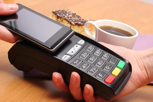 Pagando com telefone celular com tecnologia NFC para cheesecake e café no café, conceito de finanças — Fotografia de Stock