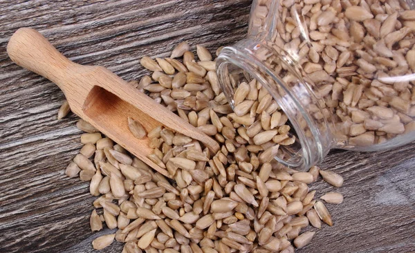 Zonnebloempitten morsen uit glazen pot. Houten achtergrond — Stockfoto