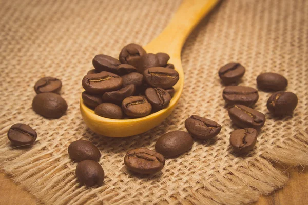 Винтажное фото, куча кофейных зерен с деревянной ложкой на холсте джута — стоковое фото